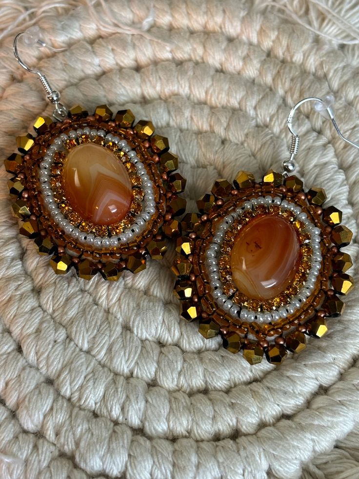 Hand made orange , pearl,  rhinestone and gold beaded dangle earrings with  orange  agate stone center. Sewn using nylon white thread. Faux leather backing. Earring hook is stainless steel. Note: small burn mark from using a flame to clean up extra thread. These were hand crafted by me. All stones and seed beads are not uniform, which gives the overall product a more authentic and "natural" touch. <3 Handmade Amber Beaded Round Earrings, Handmade Amber Round Bead Earrings, Handmade Amber Earrings With Round Beads, Handmade Adjustable Amber Earrings, Handmade Amber Agate Earrings, Orange Adjustable Beaded Drop Earrings, Adjustable Orange Beaded Drop Earrings, Elegant Beaded Agate Earrings, Handmade Oval Brown Earrings