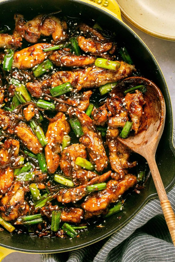 chicken and asparagus stir frying in a skillet with a wooden spoon