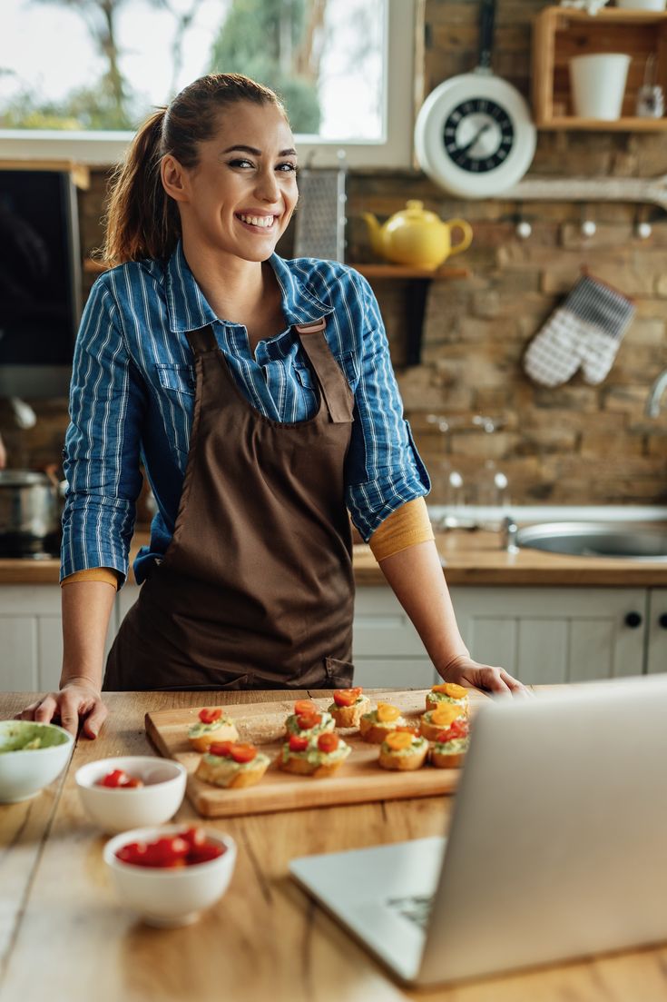 a woman standing in front of a laptop with food on the table next to her