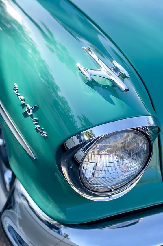 the front end of a green car with chrome trim and emblem on it's headlight