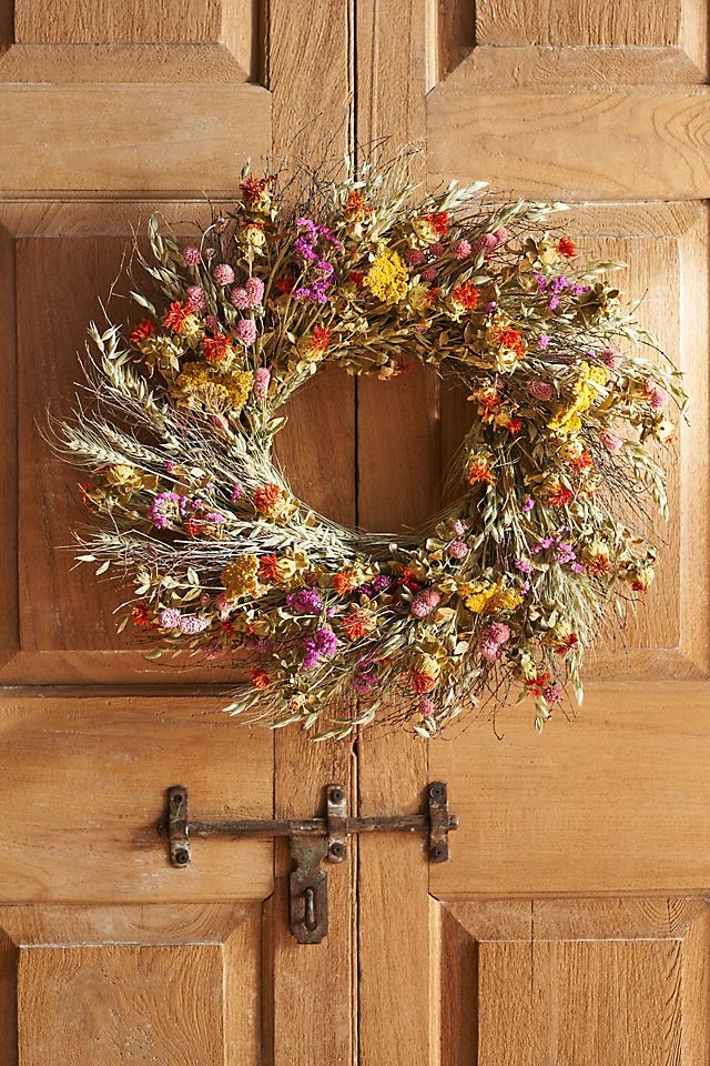 a wreath hanging on the front door of a house with dried flowers and leaves around it