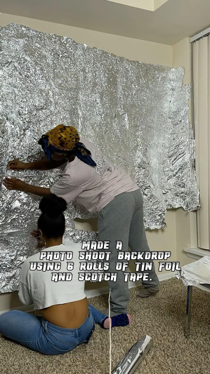 two people are working on a large piece of tin foil that is covering the wall