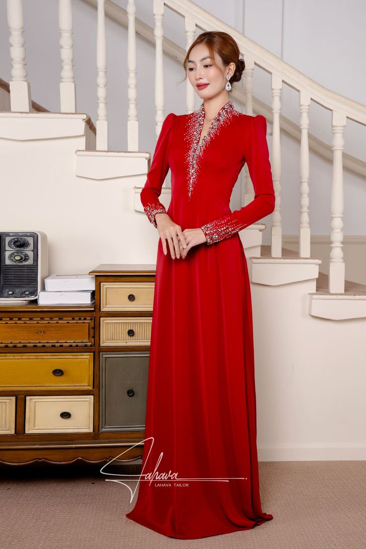 a woman in a long red dress standing next to a stair case and looking at the camera