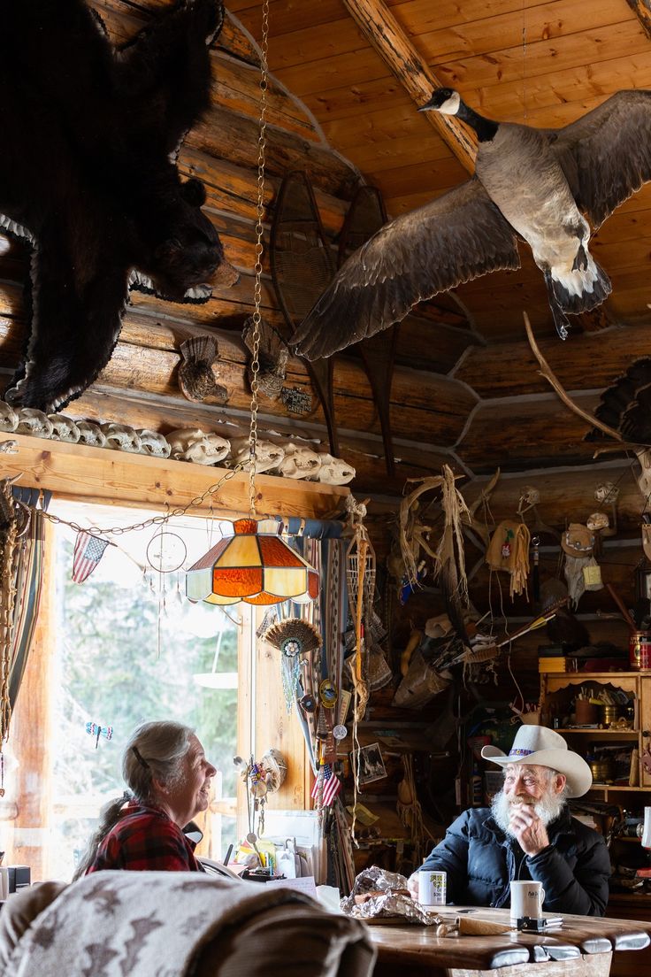 two people sitting at a table in a log cabin with birds hanging from the ceiling