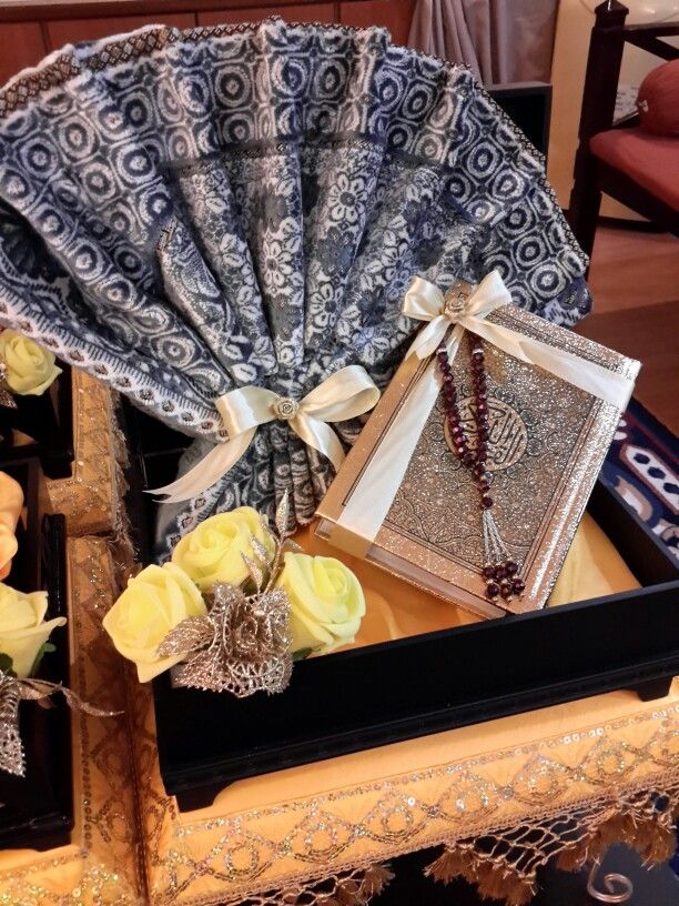 an open box with jewelry and flowers on the table in front of a decorative fan