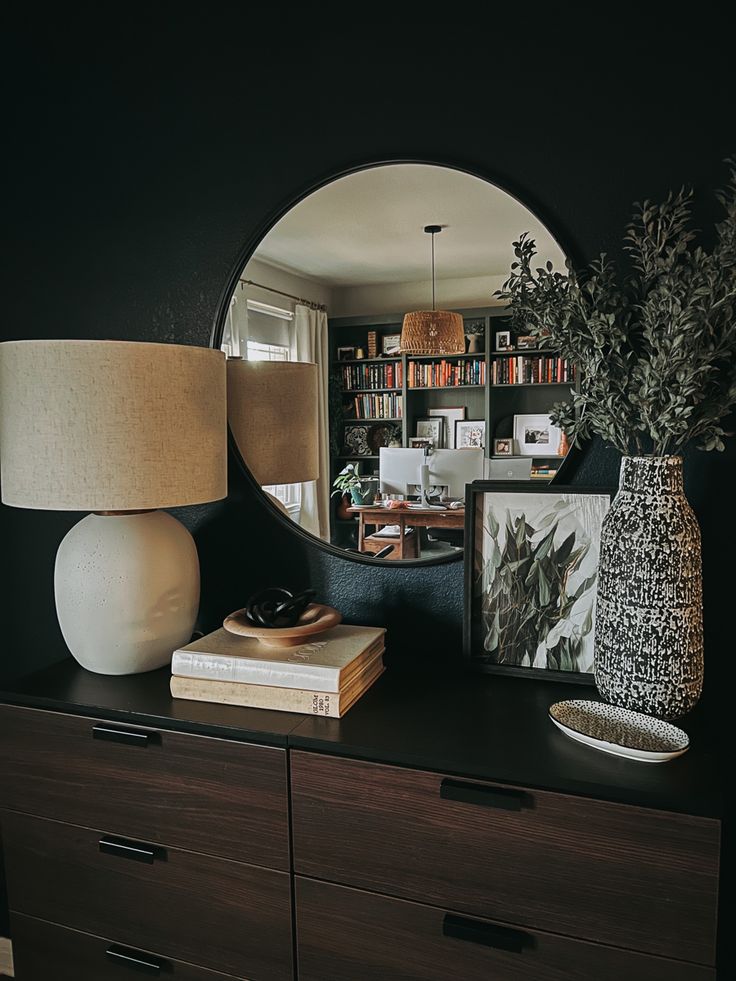 a table with a mirror, lamp and vase on it in front of a bookcase