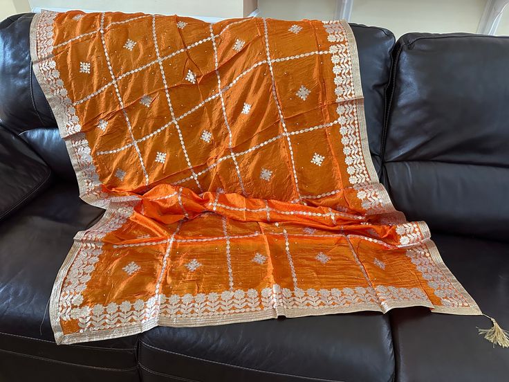 Discounted from $65.07. This is a soft, orange silk shawl scarf stole.  It has gold lace (called gota in Hindi) applique in intrinsic floral motifs throughout the wrap. Applique is sewn to the fabric so it doesn't fall off with use. All four edges have intricate sewn, gold applique as well. There are pasted stones all over the dupatta that further enhance its beauty. One tassel is on each short edge (a total of two on a dupatta).  This is a handcrafted work of wearable art. So beautiful! MATERIA Orange Silk Traditional Wear With Motifs, Festive Orange Silk Dupatta, Orange Silk Traditional Wear With Dupatta, Silk Dupatta With Zari Work In Orange, Orange Dupatta For Wedding At Eid, Orange Dupatta For Wedding And Eid, Traditional Orange Wear With Dupatta, Orange Traditional Wear With Dupatta, Orange Cutdana Dupatta For Eid