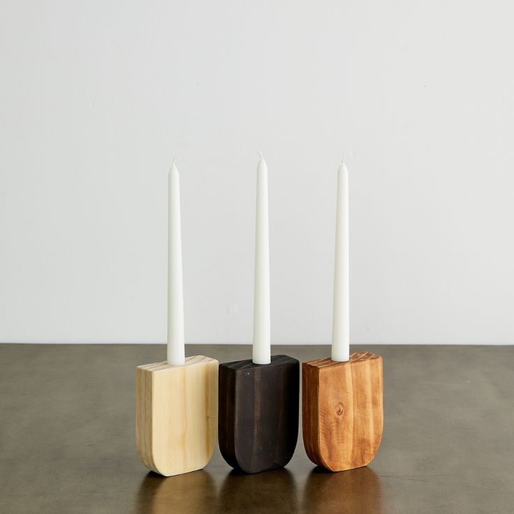 three wooden candlesticks sitting on top of a table next to two white candles