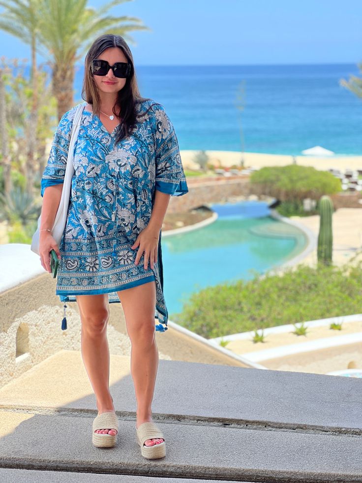 Our Aegean Blue Floral Short is an all over floral kaftan dress that is the perfect piece to dress up and wear out, wear to the beach as a cover-up, or just lounge about in it at home! This beautiful dress is named after none other than the aegean blue sea, which boasts the most gorgeous blue/teal colouring! Subtle variations in colour and pattern are to be celebrated as they are evidence of the hand made block printing and dyeing process that makes this dress unique. This dress is the epitome o Blue Boho Dress For Beach Cover-up, Blue Bohemian Resort Cover-up, Blue Printed Beach Dress For Poolside, Blue Short Sleeve Cover-up For Poolside, Blue Short Sleeve Poolside Cover-up, Bohemian Dresses For Beach Party In Resort Season, Bohemian Beach Party Dress For Resort Season, Blue Tropical Print Beachwear Dress, Blue Bohemian Cover-up For Resort Season