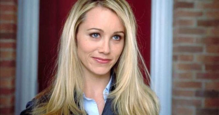 a woman standing in front of a red door with long blonde hair and blue eyes