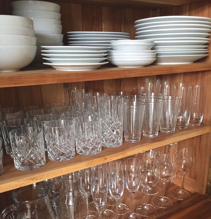 many glasses are stacked on top of each other in front of a wooden shelf filled with plates and bowls