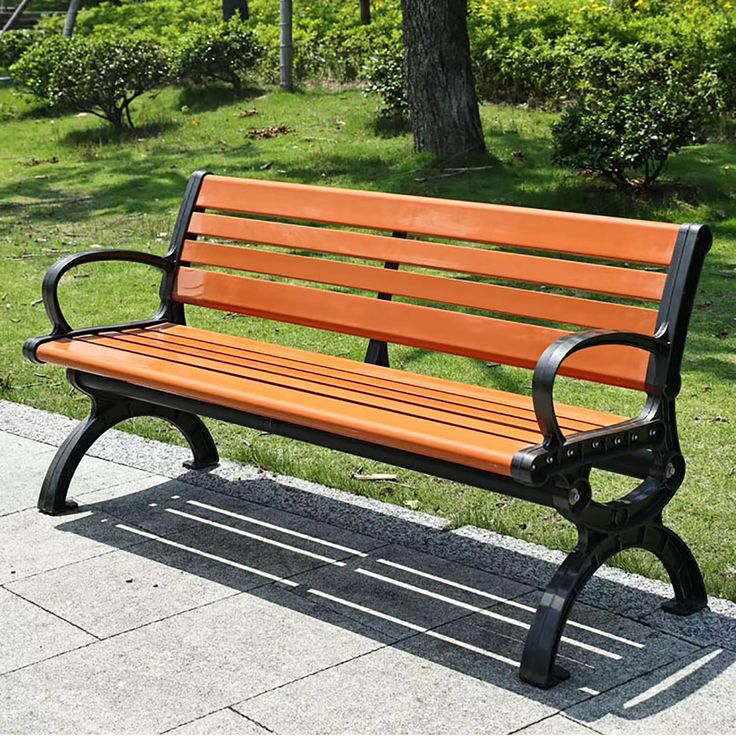 a wooden bench sitting on top of a sidewalk next to a park filled with green grass