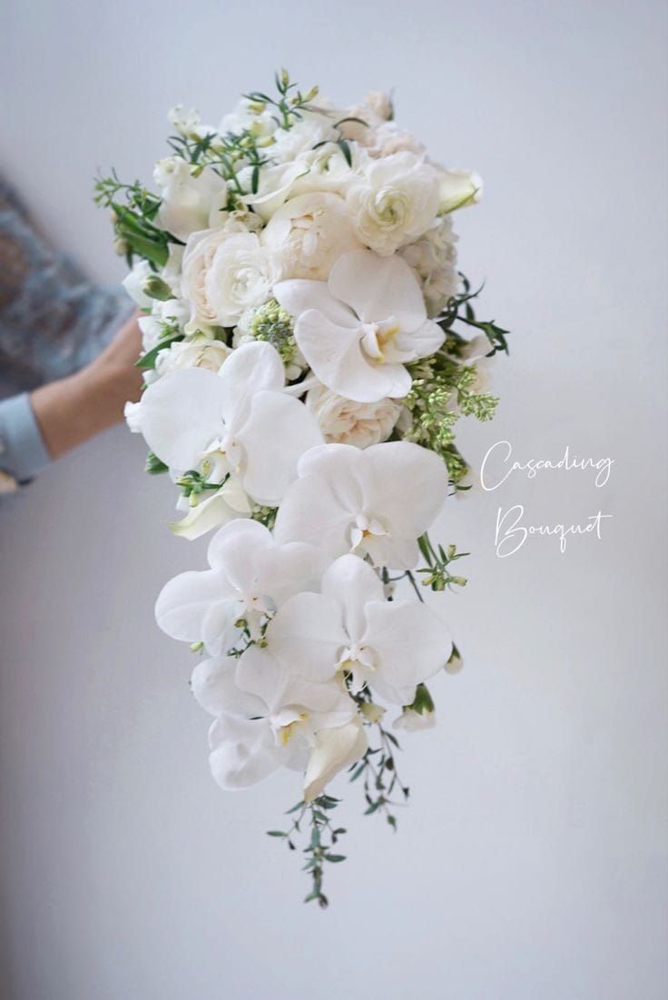 a bridal bouquet with white flowers and greenery hanging from the ceiling by someone's hand