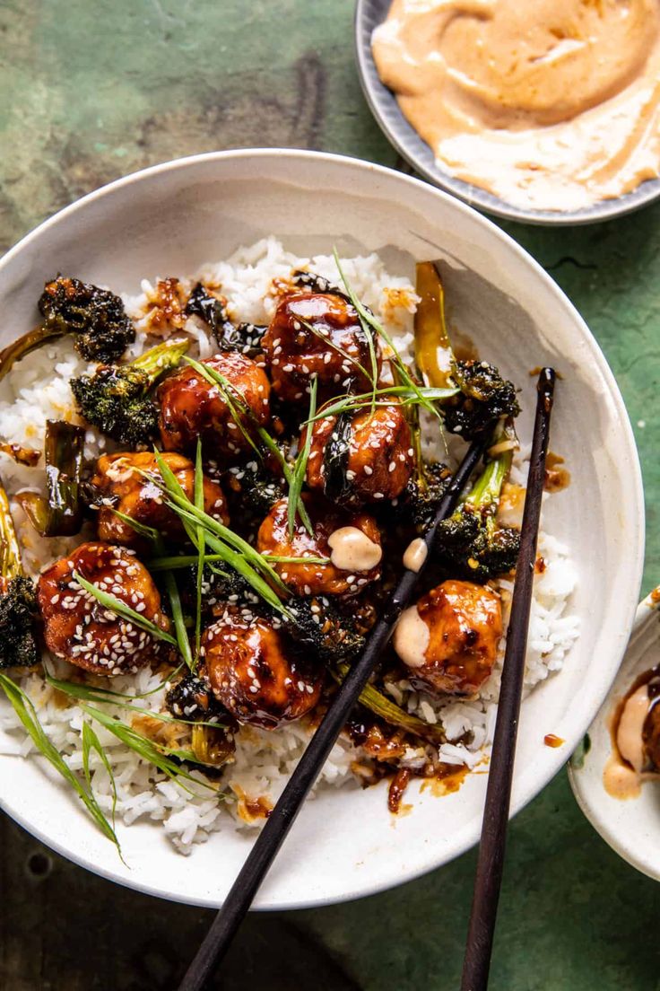 a white bowl filled with meat and vegetables on top of rice next to chopsticks