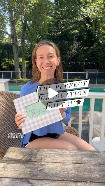 a woman sitting at a table holding up two pieces of paper that say the perfect graduation gift