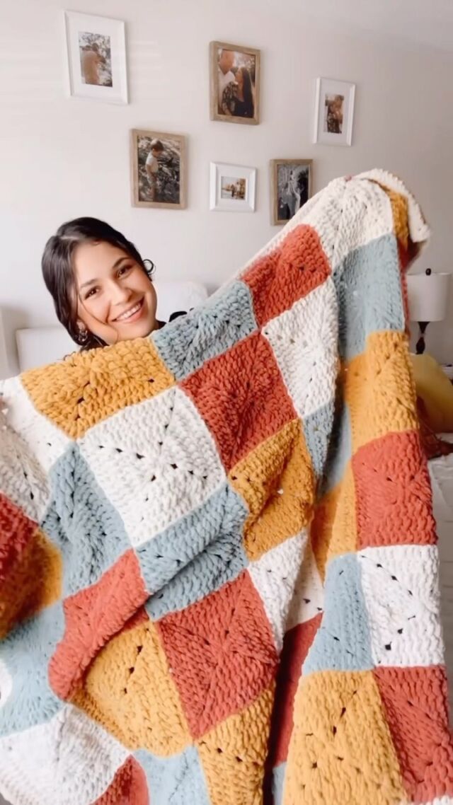 a woman laying on top of a bed covered in a colorful blanket and smiling at the camera