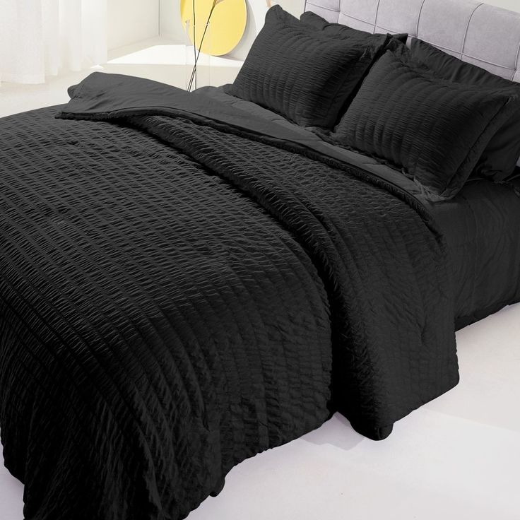 a bed with black comforter and pillows in a white room next to a yellow lamp