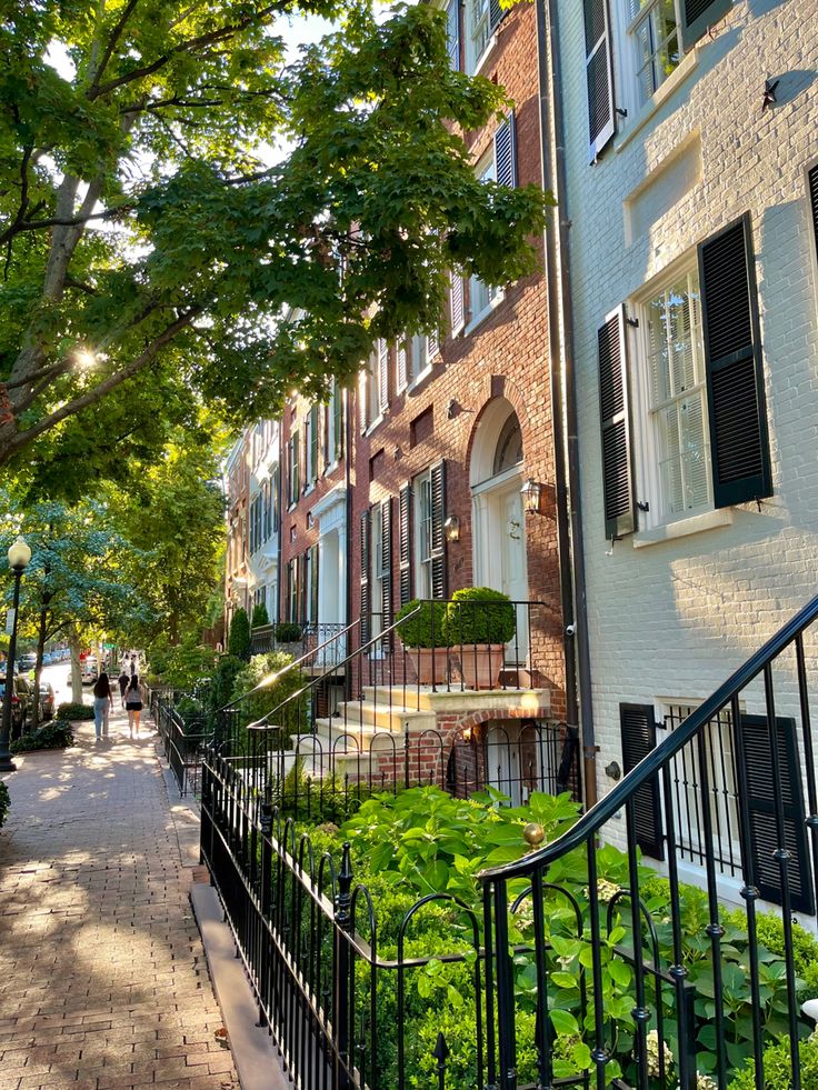 an alley way with brick buildings and green plants on either side, surrounded by trees