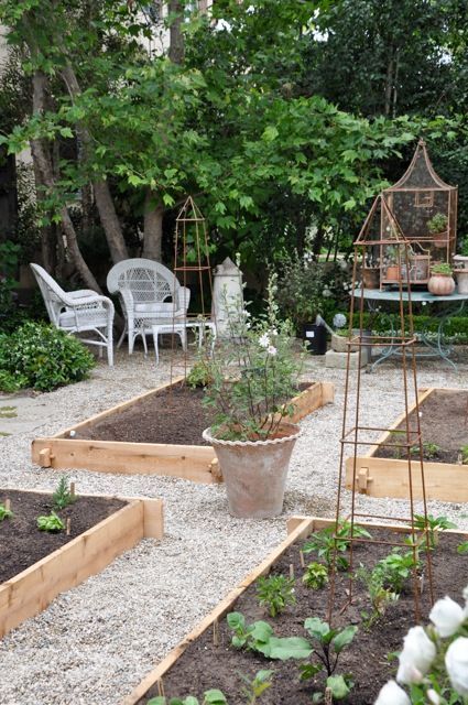 a garden with lots of plants in it and some chairs on the side walk way