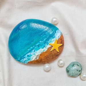 a rock with a star painted on it next to some pearls and other rocks in the sand