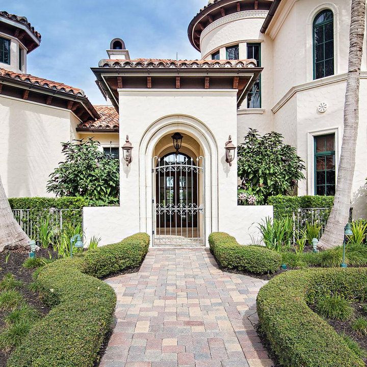 the front entrance to a large white house with hedges and bushes on either side of it