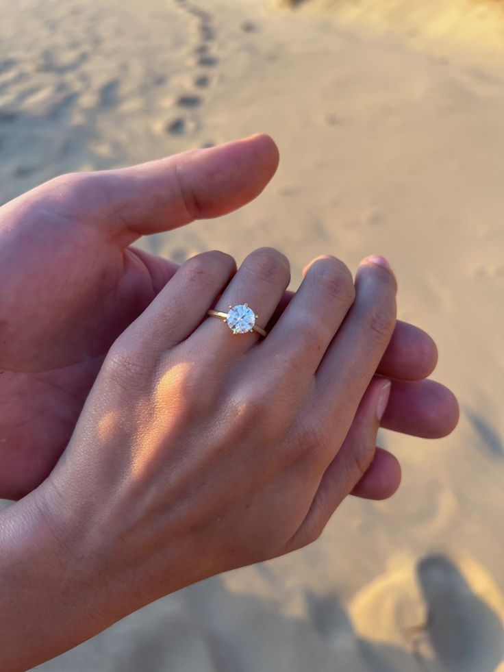 a person holding their hand in the sand with a diamond ring on it's finger