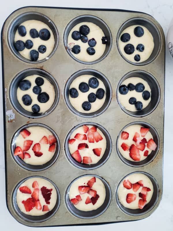 cupcakes with blueberries and strawberries are in a muffin tin on the counter