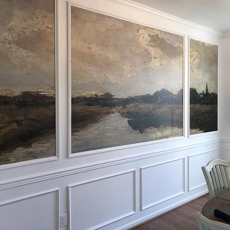 a dining room table and chairs with paintings on the wall behind them in an empty room