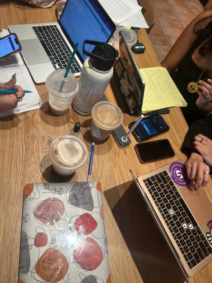 several people sitting at a table with laptops and notebooks on top of them