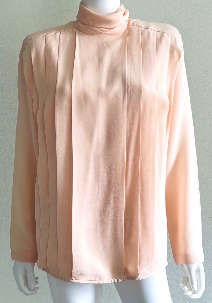 Vintage C1980s pure butter soft silk blouse from Linda Allard For Ellen Tracy in a gorgeous, delicate shade of peach or soft coral, featuring a roll neck, soft front pleats, and a rear self covered buttons closure.  Shoulder pads (removable). Approximate Measurements:      Bust: 39"; Waist: 37"; Hips: 41"; Length: 28"      Labeled a size 6 Fabric: 100% Silk Condition: Elegant C1980s blouse is in excellent vintage condition; with small marks on back, as shown. Feminine Long Sleeve Apricot Blouse, Feminine Peach Long Sleeve Blouse, Feminine Long Sleeve Peach Blouse, Elegant Fitted Peach Blouse, Shades Of Peach, Soft Coral, Ellen Tracy, Roll Neck, Blouse Top