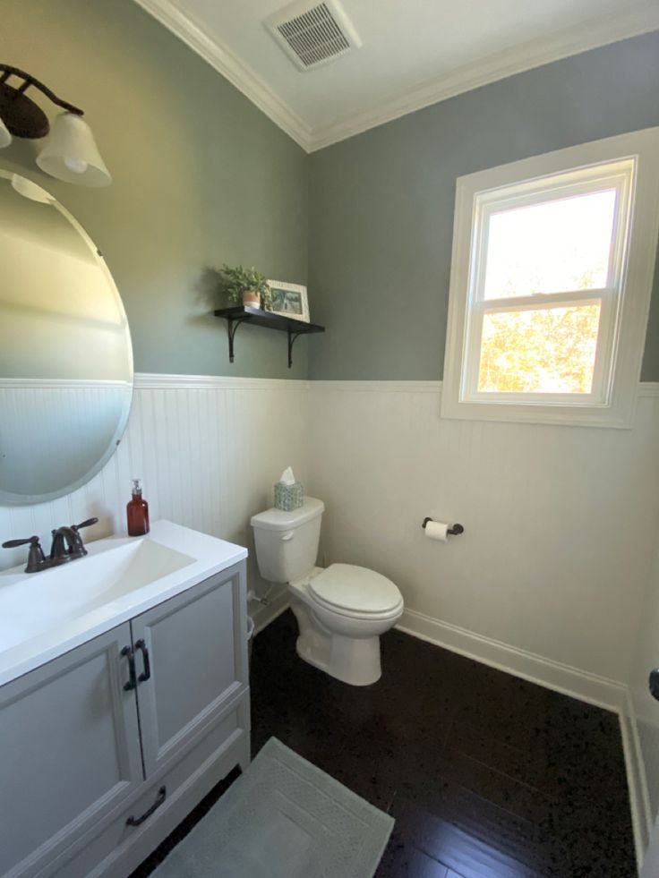 a white toilet sitting next to a sink in a bathroom under a large round mirror