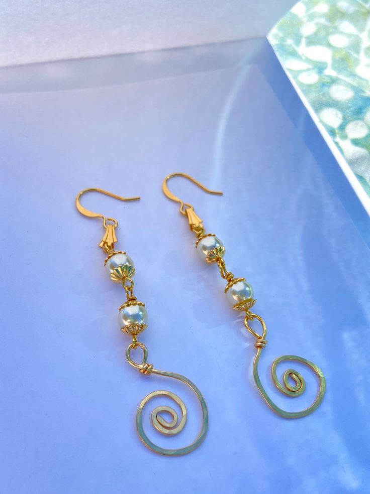 Elegant Pearl and Gold Earrings featuring a lightly hammered gold wire swirl design ~ One-of-a-kind earrings hammered smooth, with gold swirls paired beautifully with ivory pearls ~ Lightweight and elegant look makes it perfect for any formal occasion and dainty enough to wear casually\ ~ Can be customized for gold or silver and can feature 1-3 pearls (if choosing silver: the wire swirl and earring loop will be silver, but the caps around the pearls will remain gold!) ~ Handmade jewelry by Outer Banks artist - Smidge Art by Savannah Midgette Gold Swirl Wire Wrapped Earrings, Elegant Swirl Wire Wrapped Earrings, Handmade Spiral Gold Earrings, Handmade Gold Spiral Earrings, Gold Swirl Metal Earrings, Gold Swirl Earrings For Pierced Ears, Gold Wire Dangle Earrings, Spiral Wire Earrings With Ear Wire, Gold Wire Wrapped Swirl Jewelry