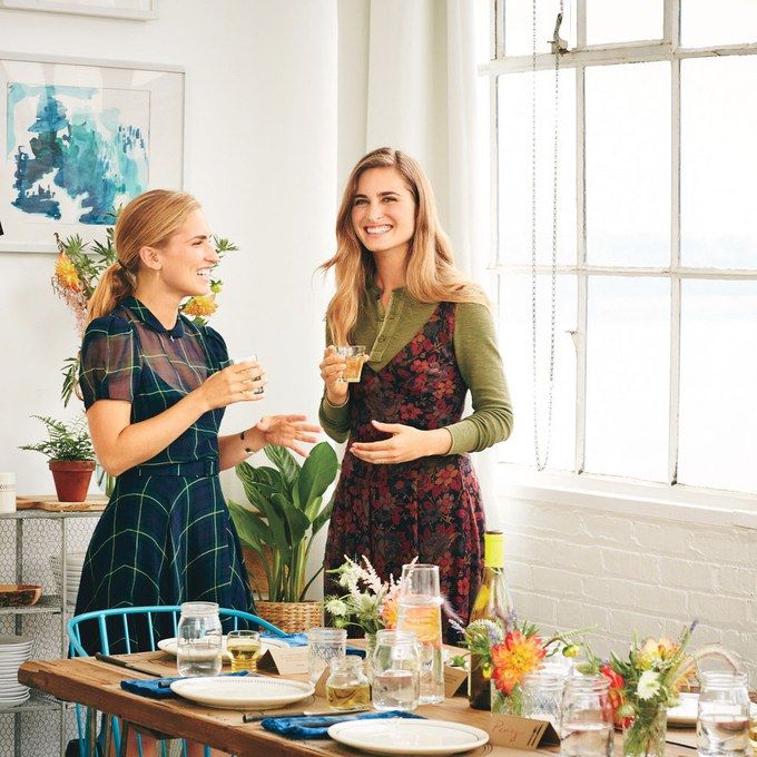 two women standing at a table with food and drinks