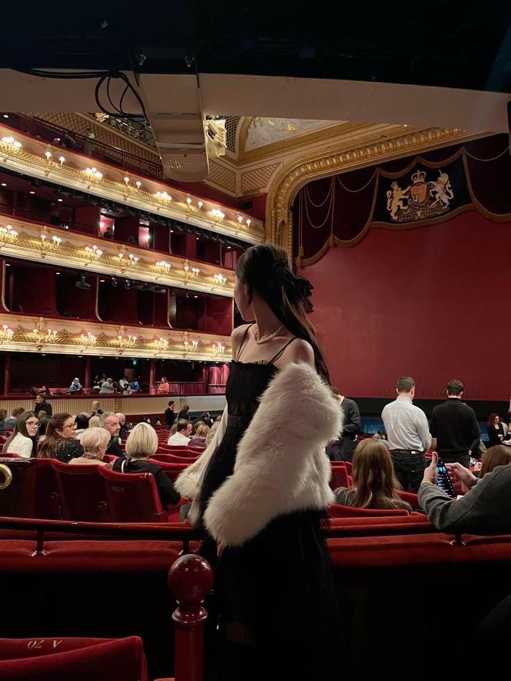 a woman standing in front of an auditorium with red seats and people sitting on the stage