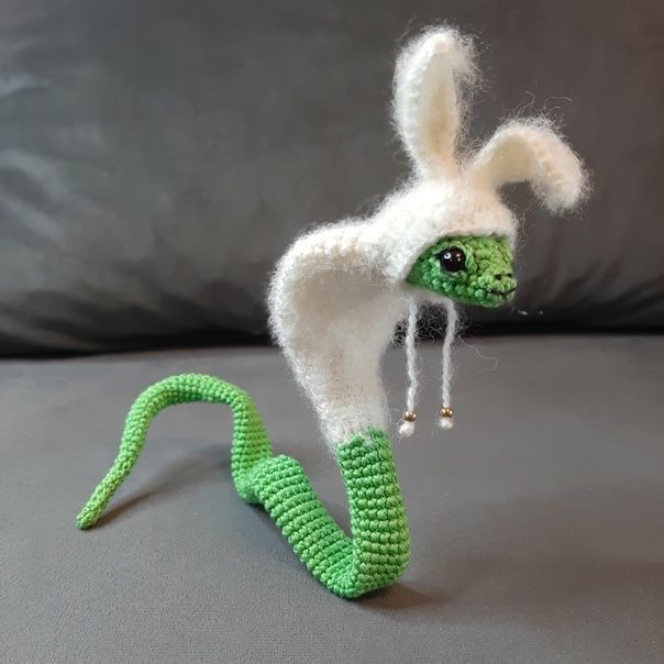 a green and white knitted animal on a gray surface next to a black pillow