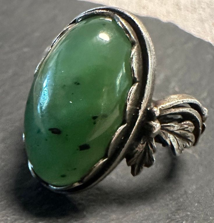 A vintage silver Genuine nephrite or Siberian Jade Decorative ring.  Size. 5 1/3, wt.- 5.5 grams, scalloped bezel set oval jade is approx. 11 x 17mm.  Lovely attention to details, hand textured silver with sculptural floral shoulders-very well made in very good condition. Antique Emerald Ring Oval Cabochon, Antique Emerald Ring With Oval Cabochon, Antique Oval Emerald Ring, Collectible Oval Cabochon Emerald Ring, Unique Oval Cabochon Emerald Ring, Oval Jade Jewelry With Large Stone, Art Deco Green Oval Emerald Ring, Antique Oval Collectible Rings, Unique Oval Emerald Ring With Polished Finish