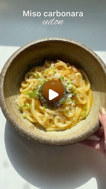 a person holding a wooden bowl filled with pasta and an egg on top of it