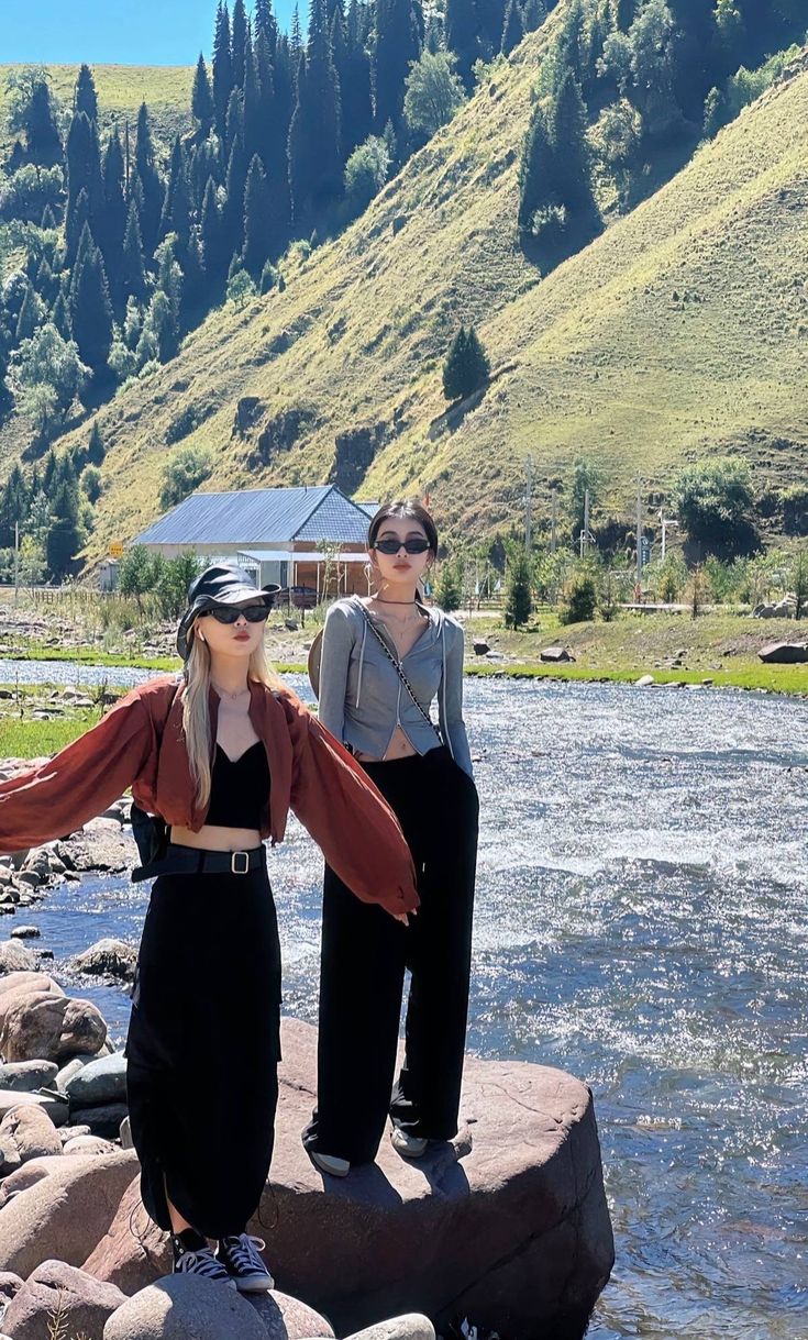 two women standing next to each other on rocks in front of a river and mountains