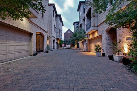 an empty brick street with two garages on each side and trees in the middle