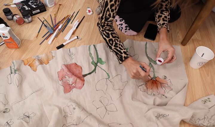 a woman is painting flowers on a sheet with watercolors and paintbrushes