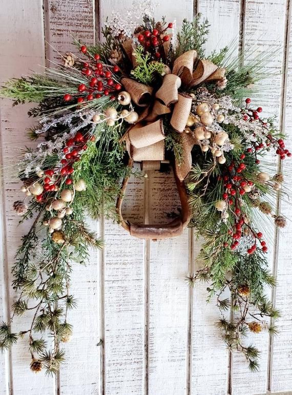 a christmas wreath hanging on the side of a white wooden wall with pine cones and berries