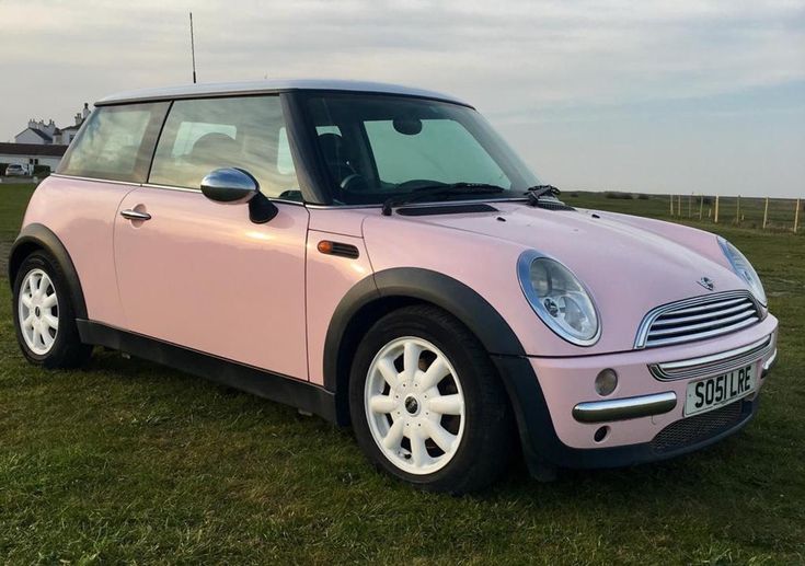 a small pink car parked on top of a lush green field