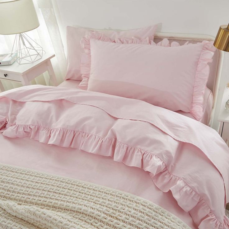 a pink bed with ruffled sheets and pillows