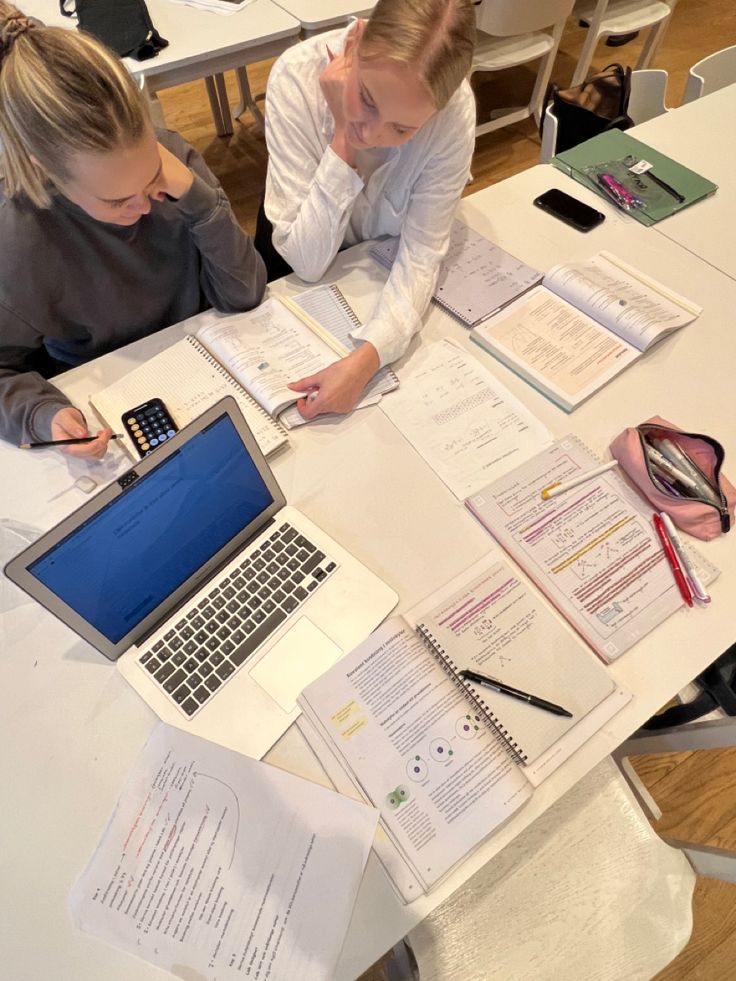 two women sitting at a table with open notebooks and papers on top of them