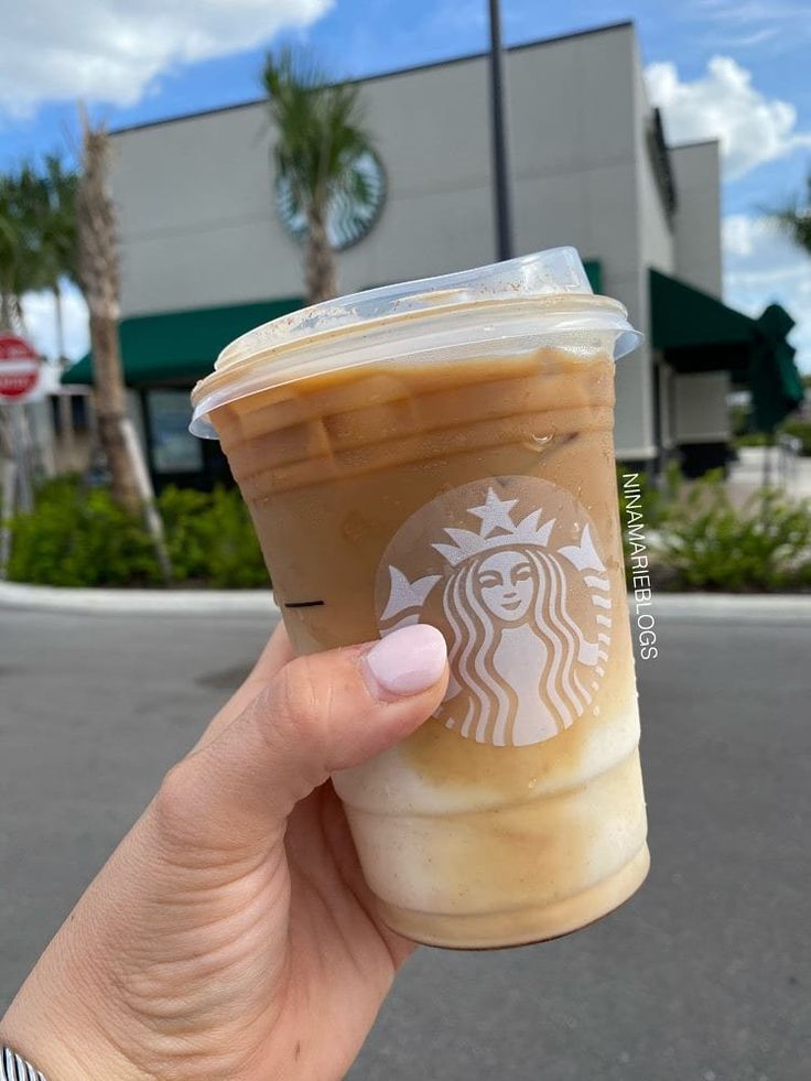 a hand holding up a cup of coffee in front of a starbucks building with palm trees