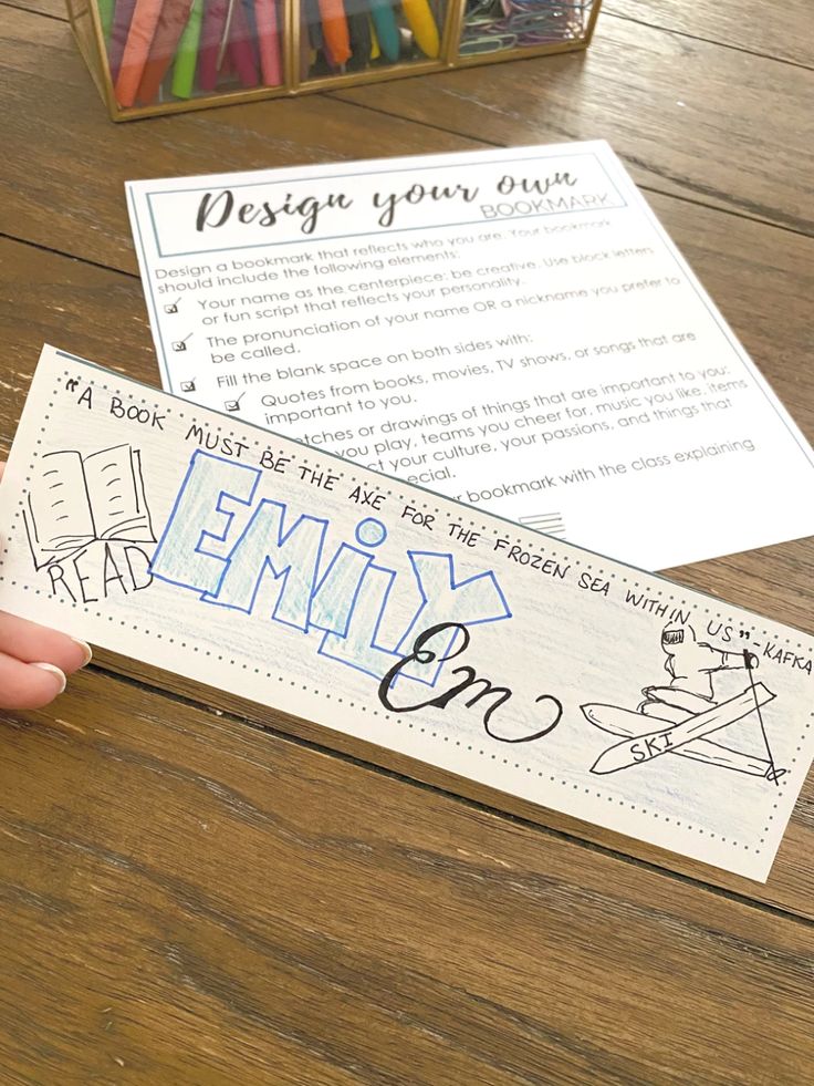 a person holding up a bookmark with writing on it next to a box of crayons