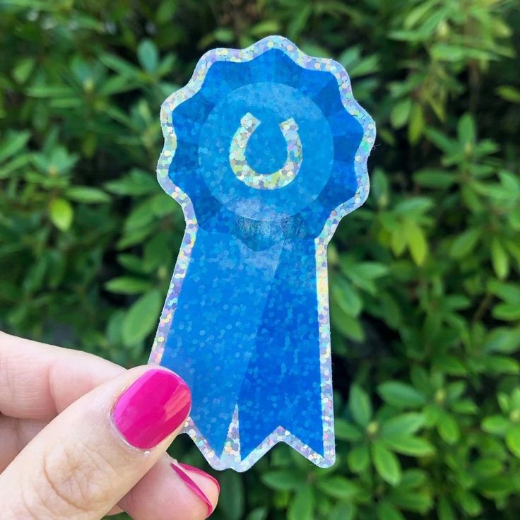 a person holding up a blue sticker with the letter c on it in front of some bushes