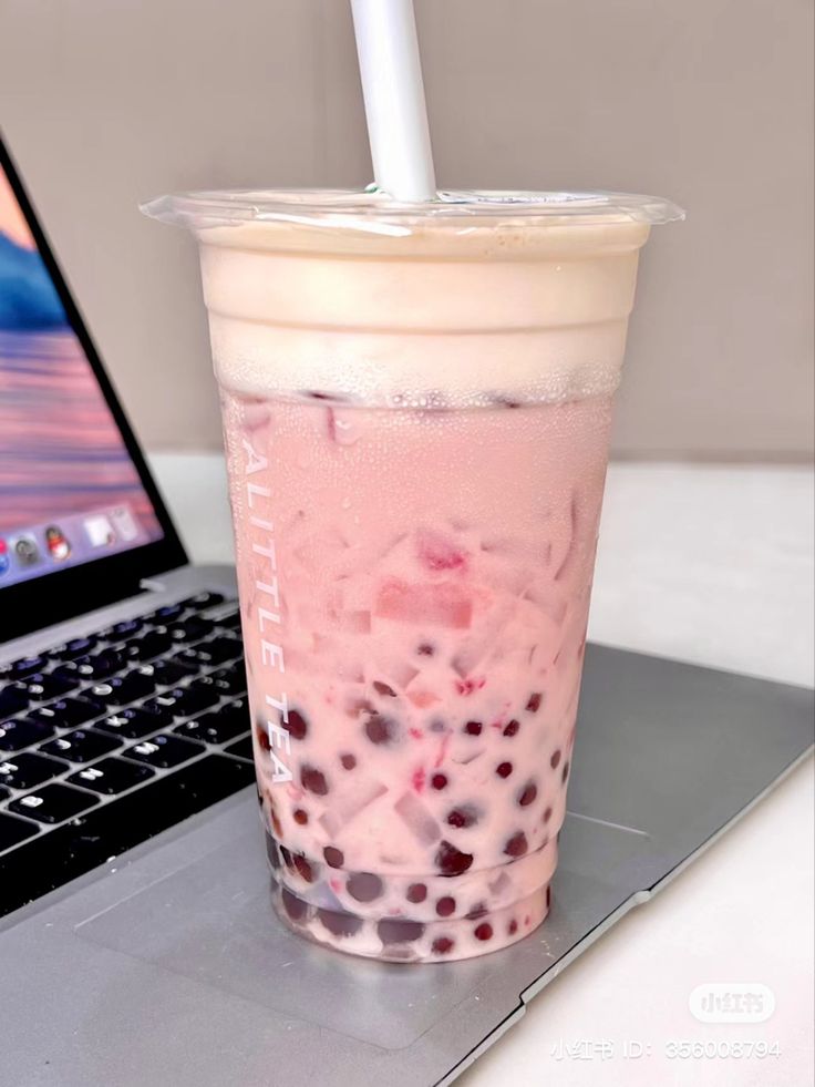 a drink sitting on top of a laptop computer next to a cup with a straw in it