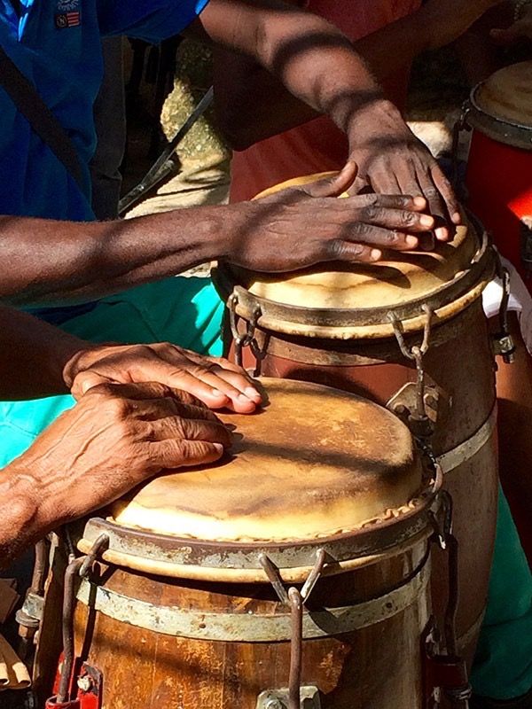 two hands on top of drums with people in the background behind them and one hand reaching for it