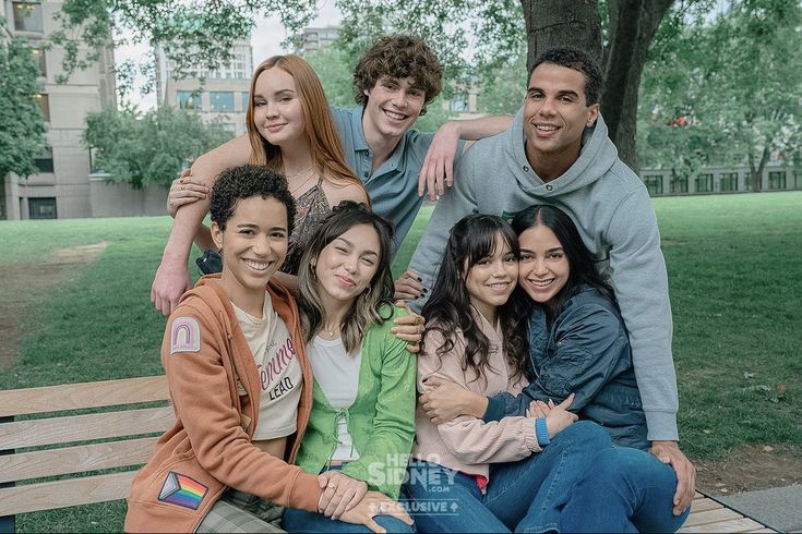 a group of young people sitting on top of a wooden bench in a city park